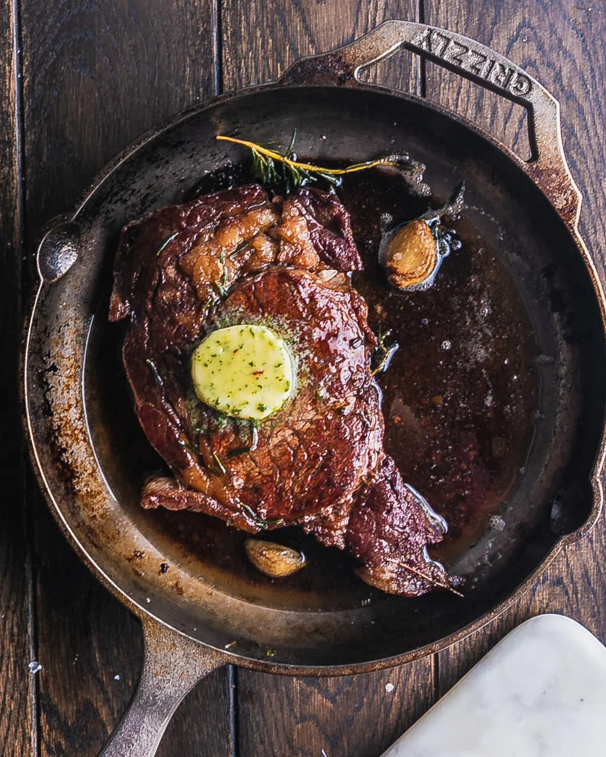 overhead view of a reverse seared ribeye steak in a cast iron pan wit ha pat of compound butter on top