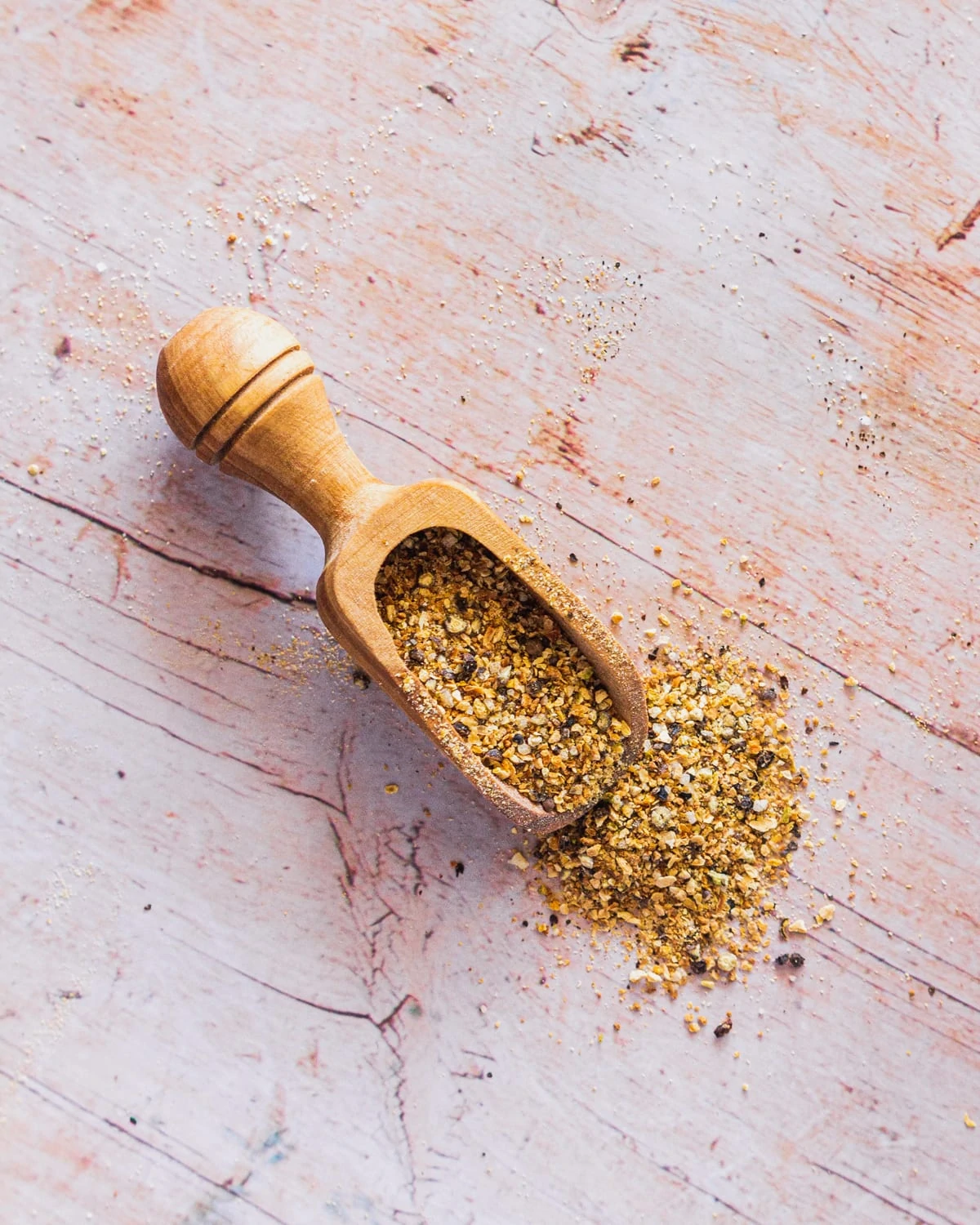 a wooden scoop filled with homemade lemon pepper seasoning spilling onto a white wood surface